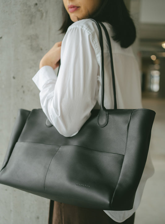Person holding a black leather tote bag in an indoor setting